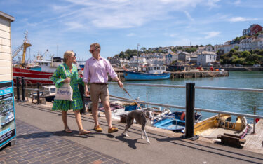 Couple walking dog around dog-friendly Brixham Harbour